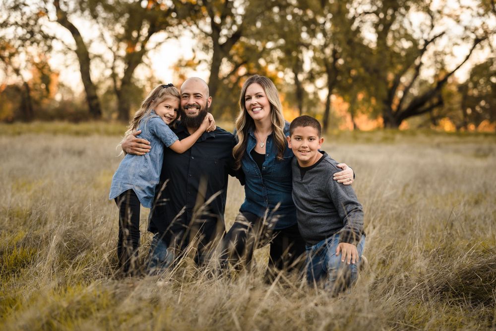 A family group poses together in tall autumn grass during golden hour.