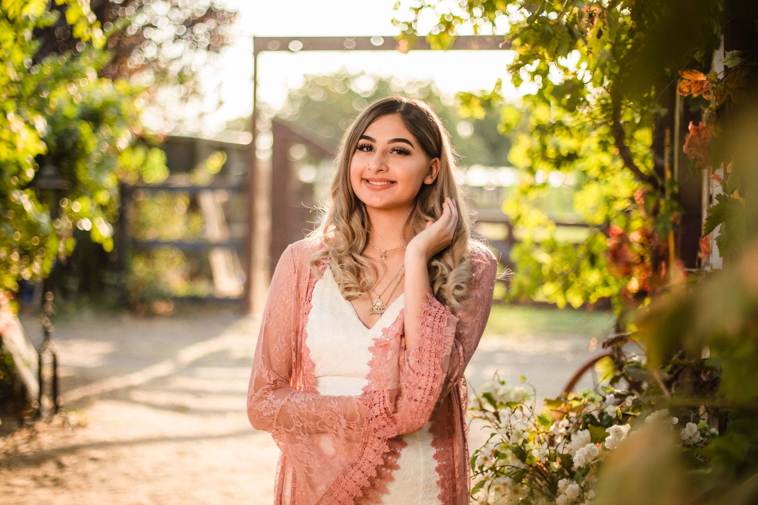 A sunset portrait in a pink lace cardigan with golden sunlight filtering through trees.