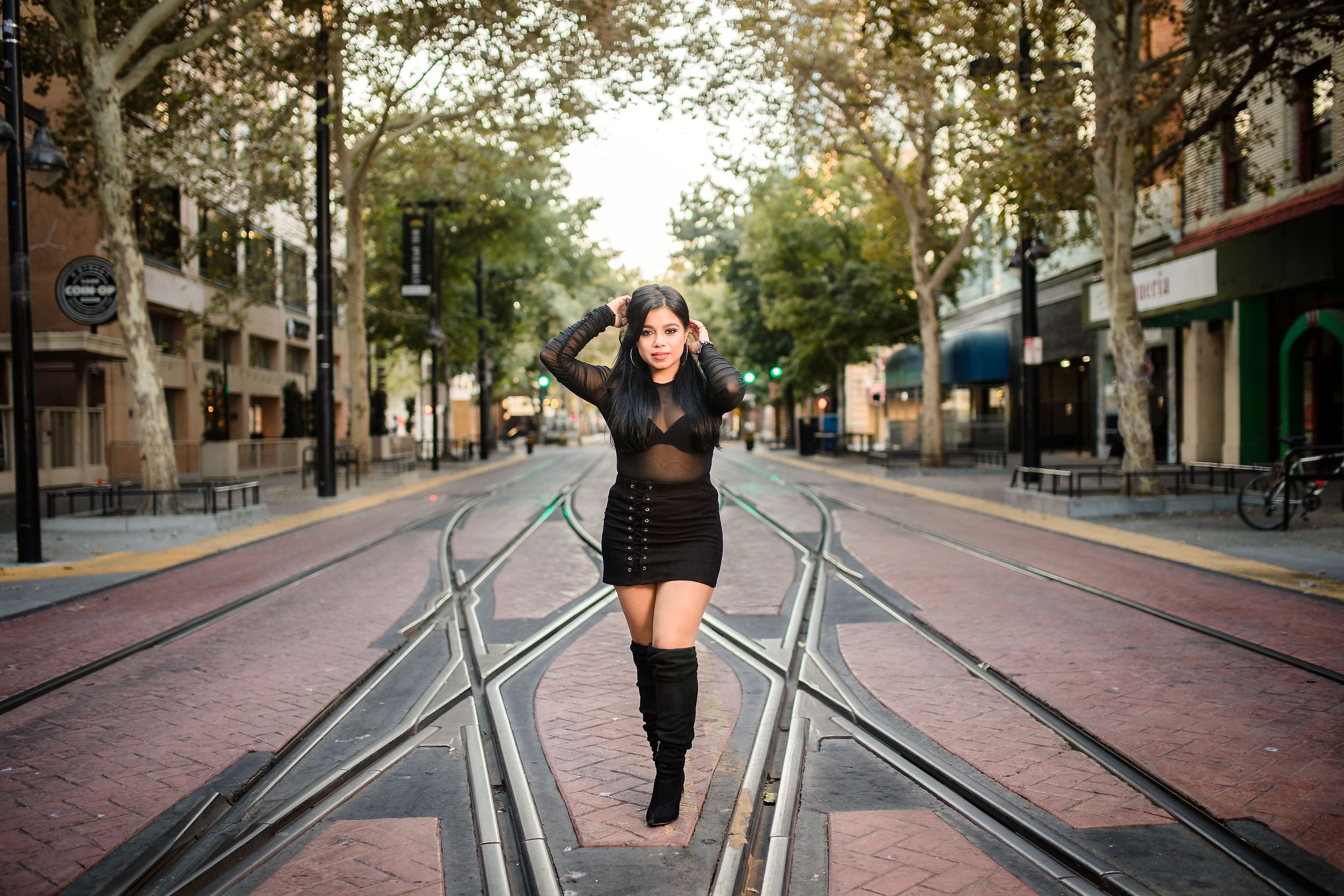 A fashion portrait on urban train tracks with black boots and dress in a downtown setting.