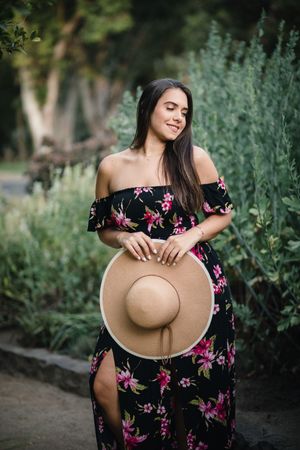 A summer portrait featuring a floral dress and straw hat among garden greenery.