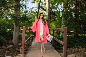 A fashion portrait on a wooden bridge featuring a bright coral jacket and designer handbag.