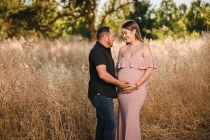 Maternity portrait in tall golden grass during sunset featuring pink maxi dress.