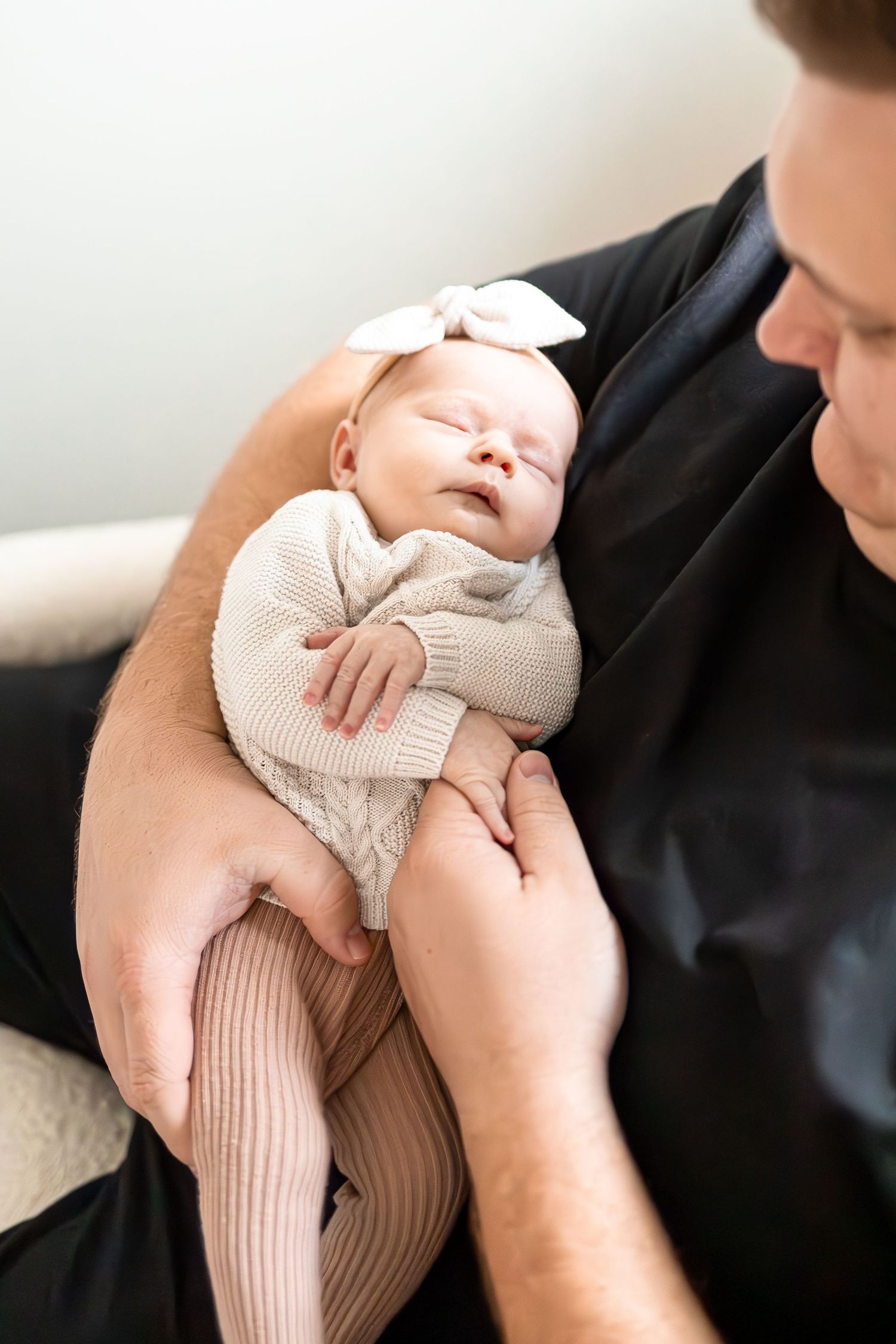 A sleeping newborn in a cream-colored outfit is held gently in their caregiver's arms.