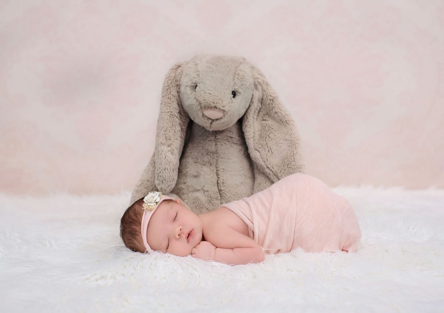 Sweet newborn portrait with large plush bunny on white textured backdrop.