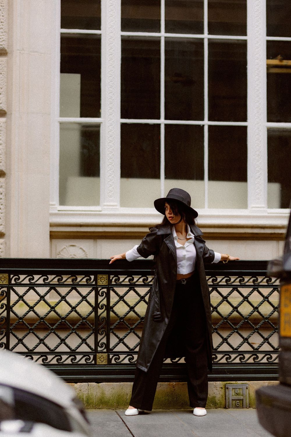 Person in black attire lounging on an ornate railing outside a classic building.
