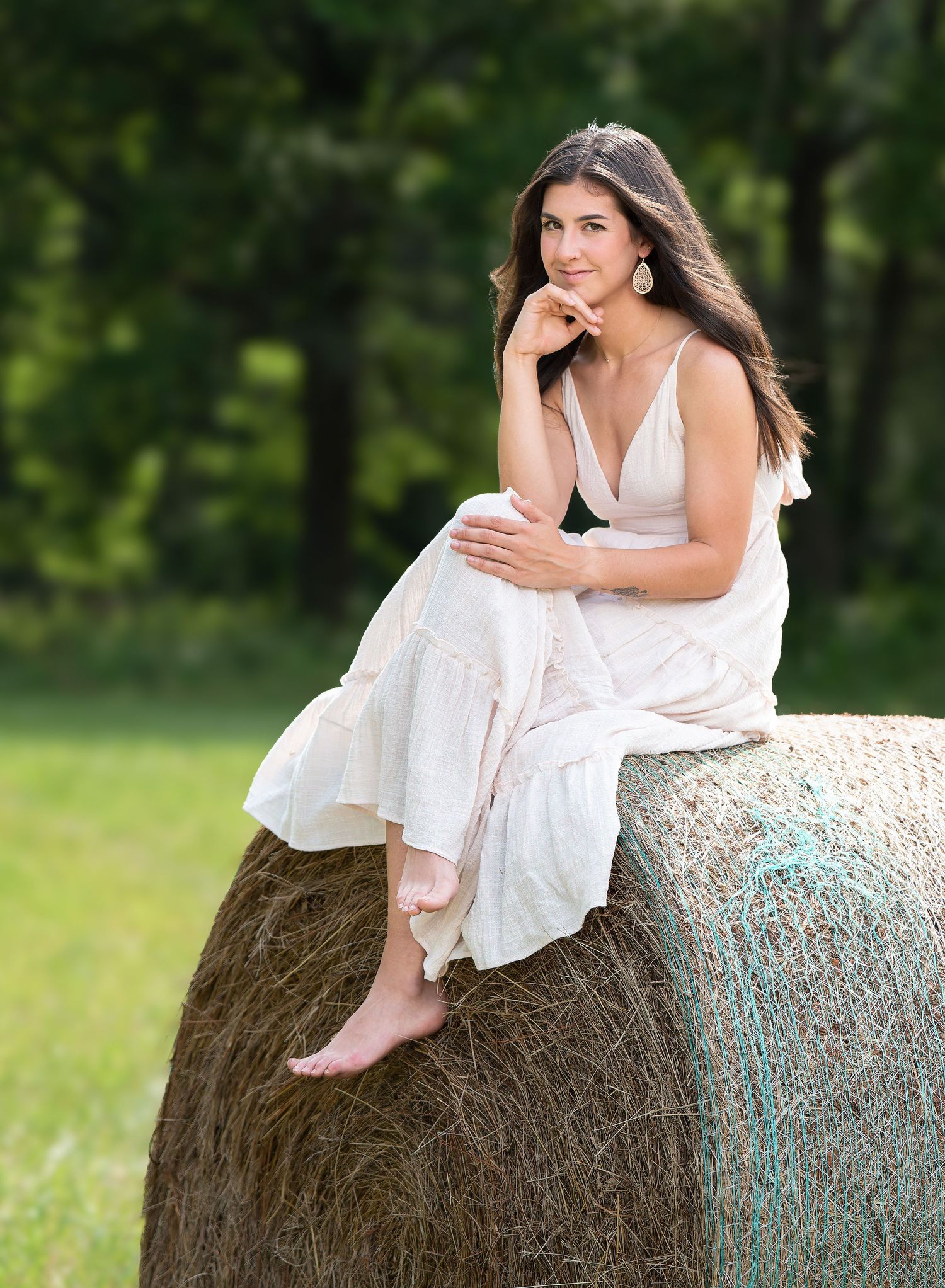 A woman in a white summer dress sitting on a hay bale in a sunny Mid-Missouri field, enjoying a peaceful countryside portrait moment.