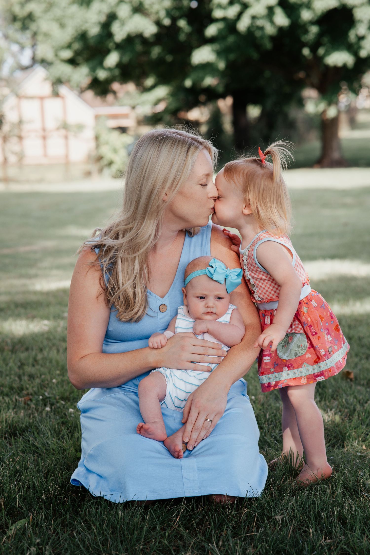 Sweet outdoor family moment with mother and children sitting on grass in summer.