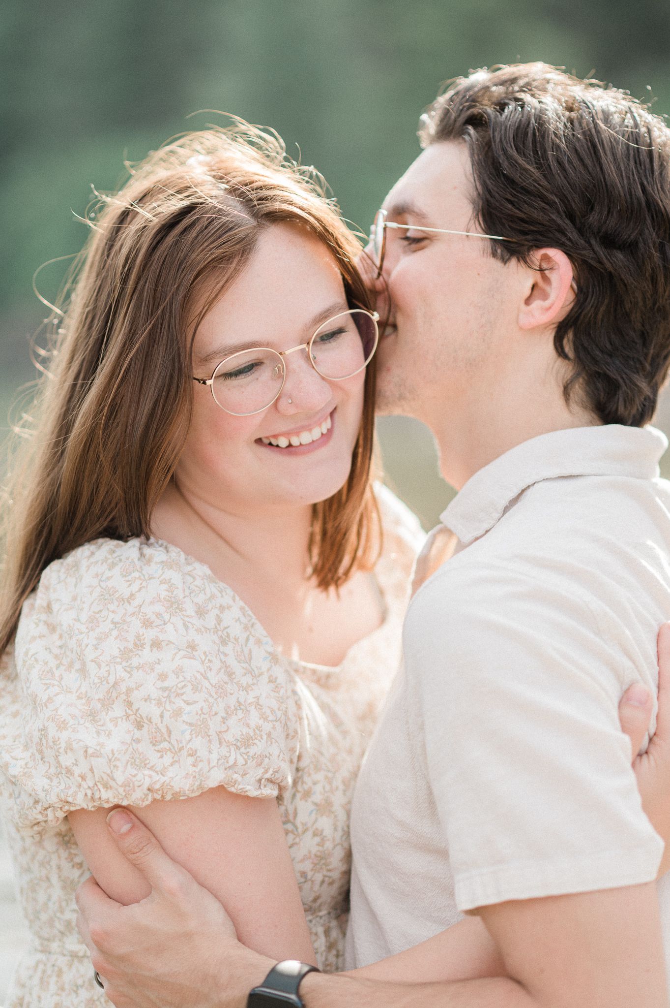 A couple in white attire share an intimate moment in a sun-drenched outdoor setting.