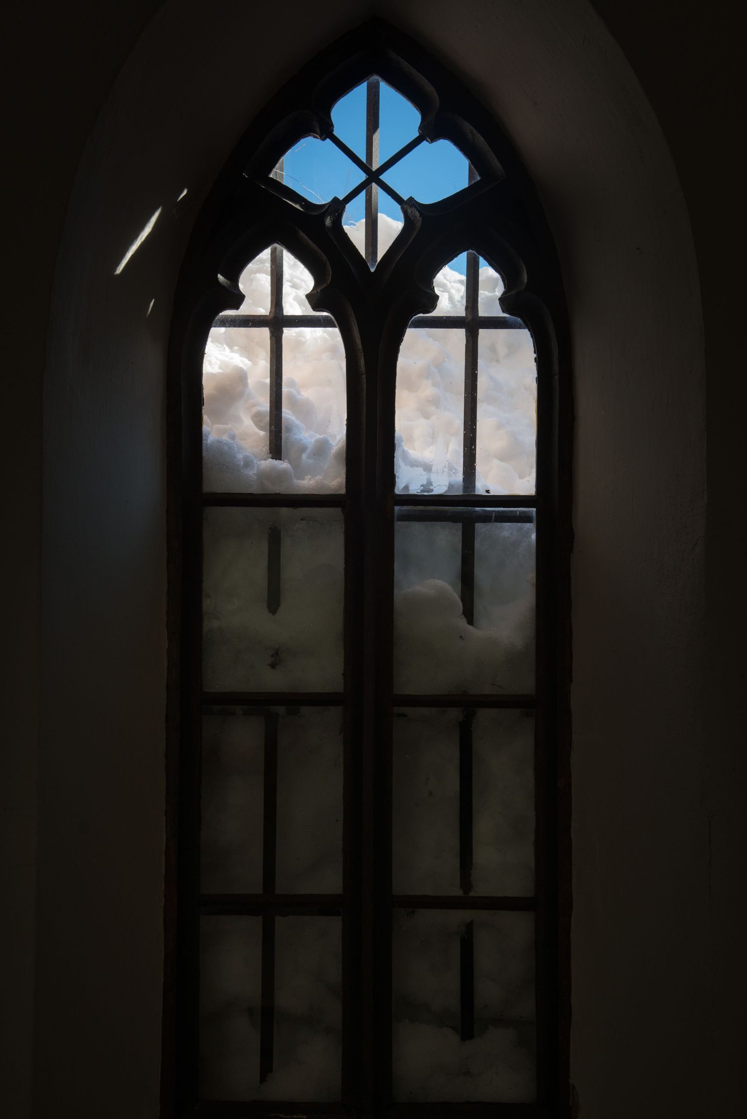 Gothic church window with quatrefoil design showing blue sky through frosted glass.