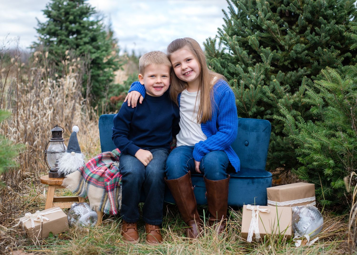 Two people sit on a blue bench surrounded by Christmas trees and decorative gift boxes.