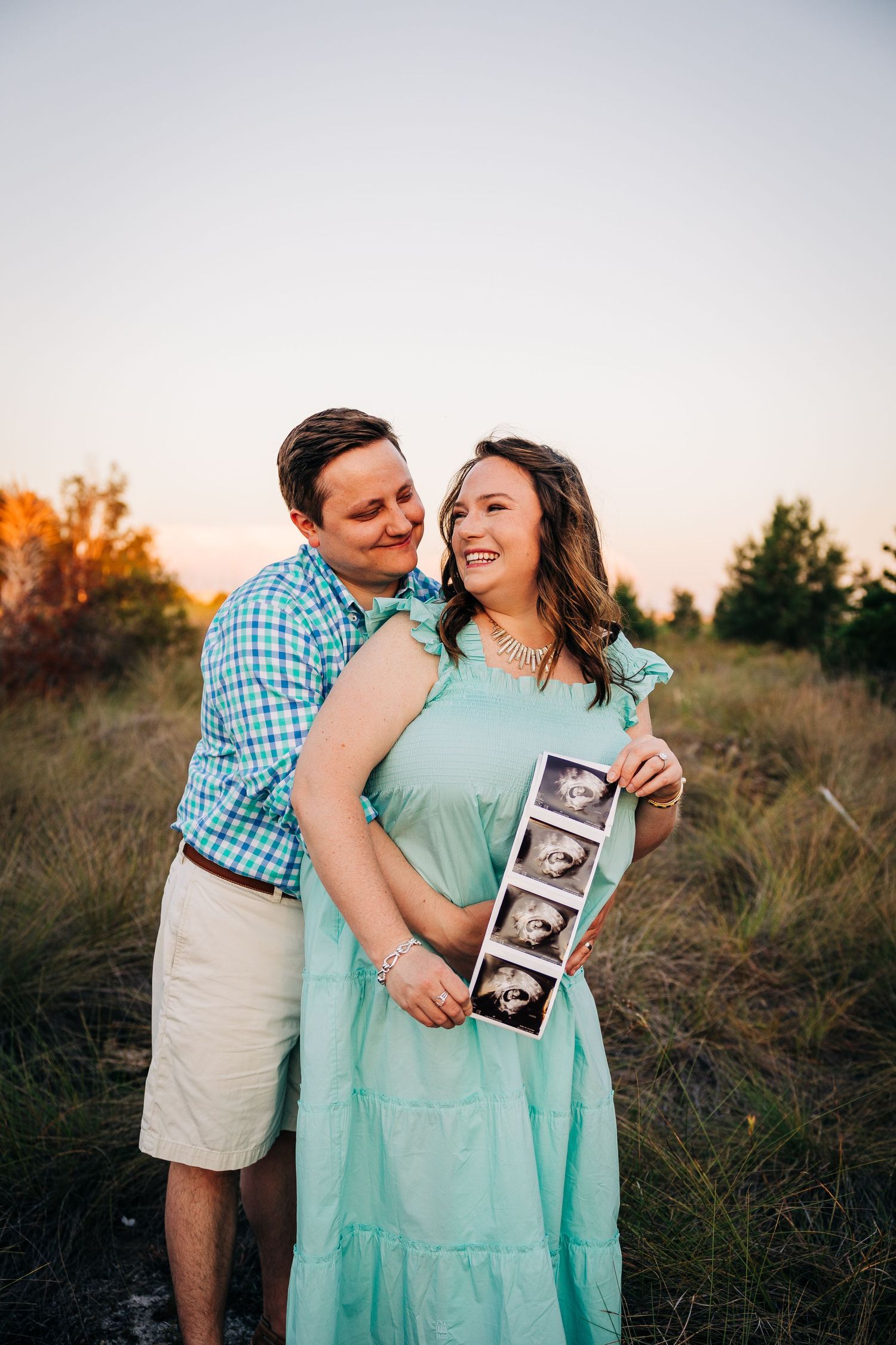 Pregnant couple holding sonogram at sunset on Siesta Key beach for maternity session taken Sarasota Family Photographer.