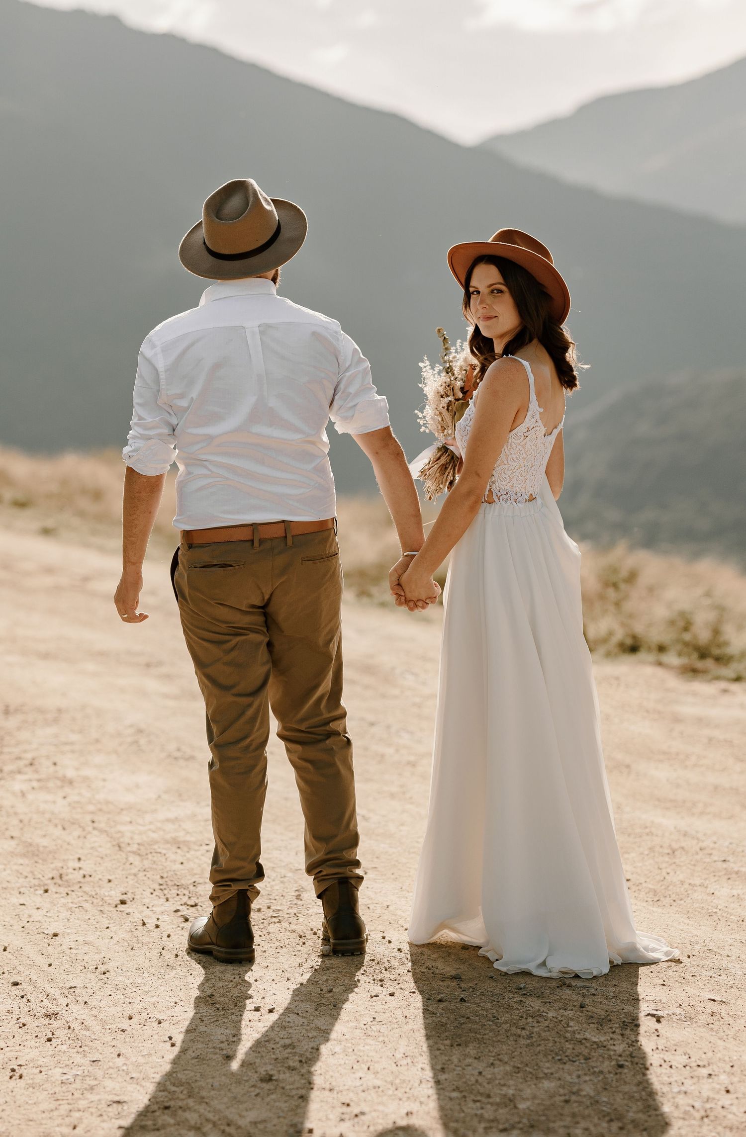 Couple in western attire pose against mountainous backdrop on their wedding day.
