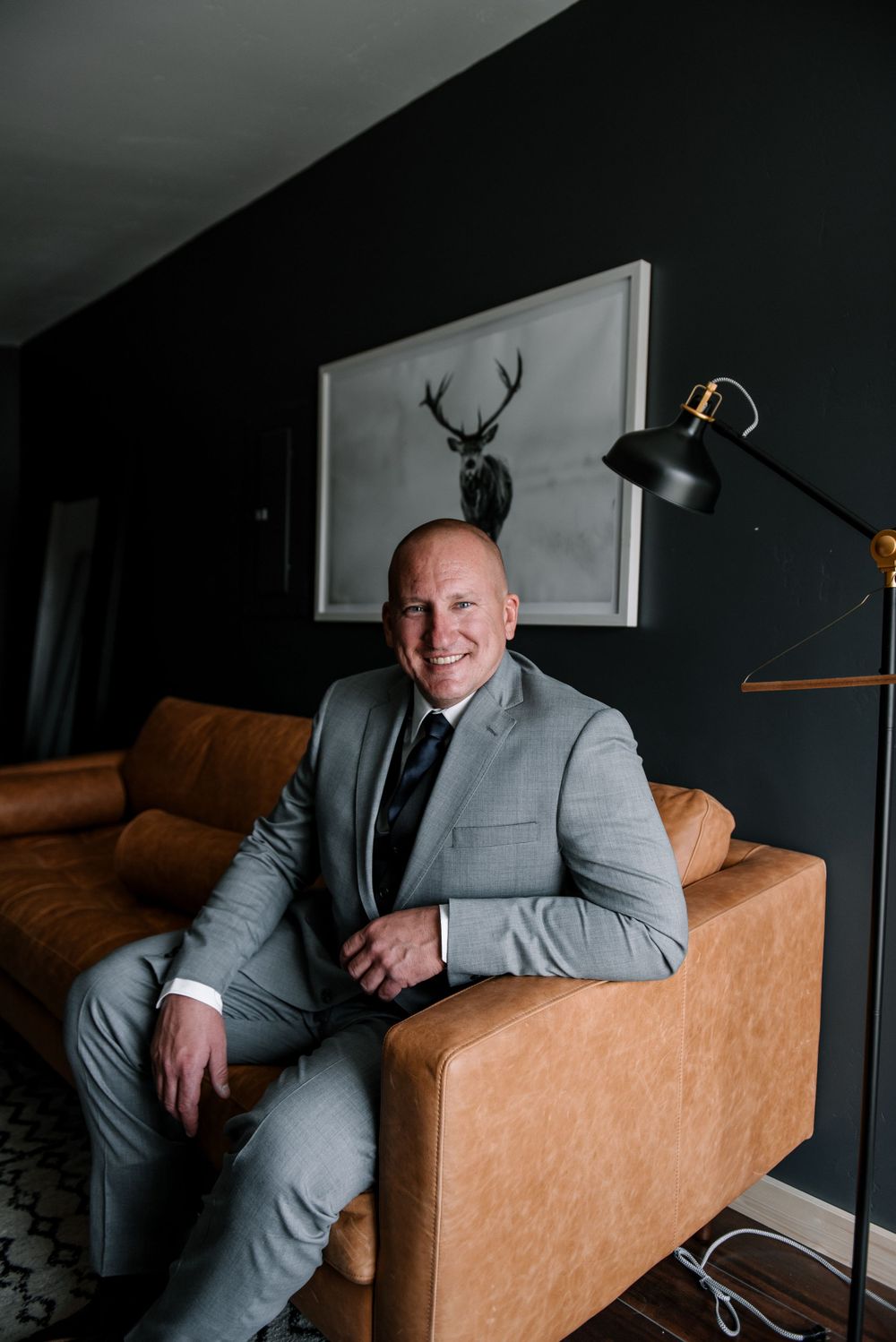 Stylish grey suit against dark walls and tan leather couch in contemporary setting.