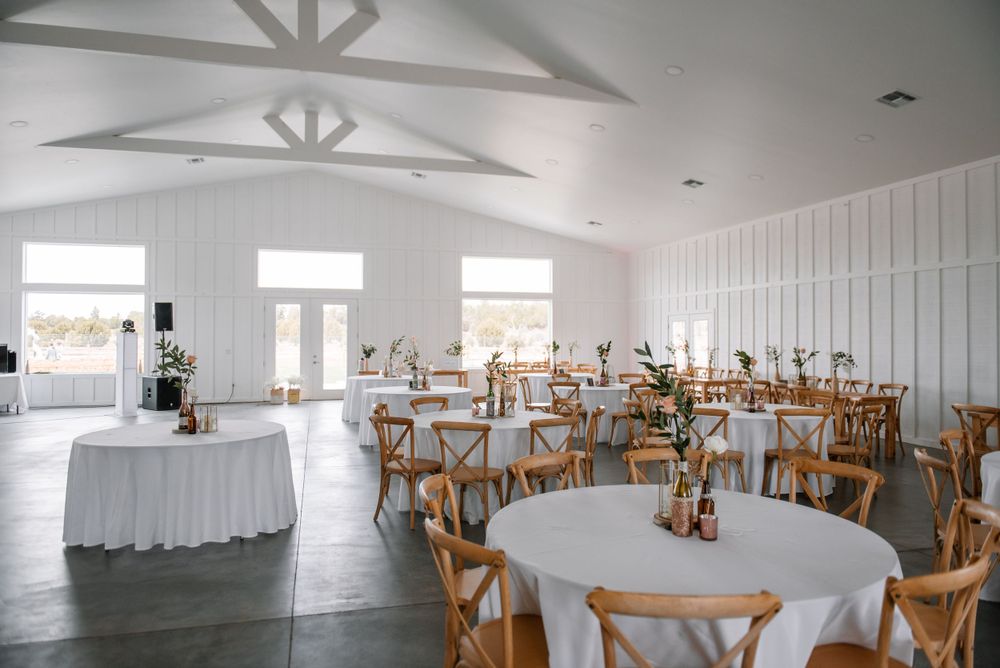 Bright white reception venue with wooden cross-back chairs and vaulted ceiling details.