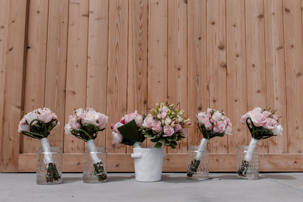 Delicate pink floral arrangements displayed on wooden shelves against a rustic fence backdrop.