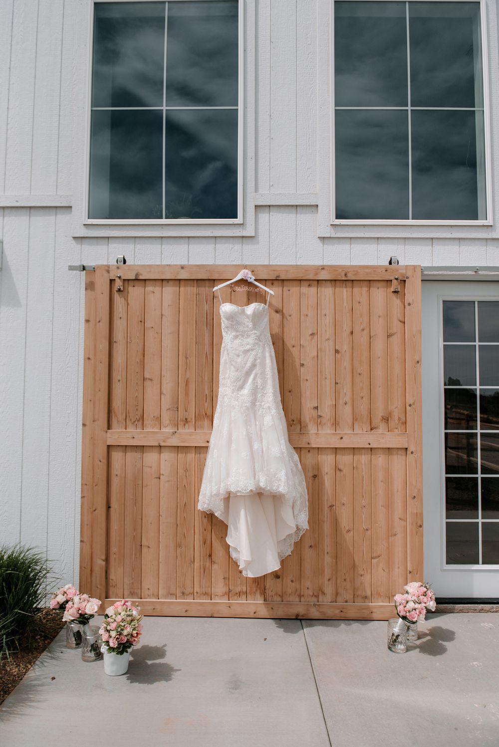 White wedding dress displayed against a modern building exterior with wooden fence panels.