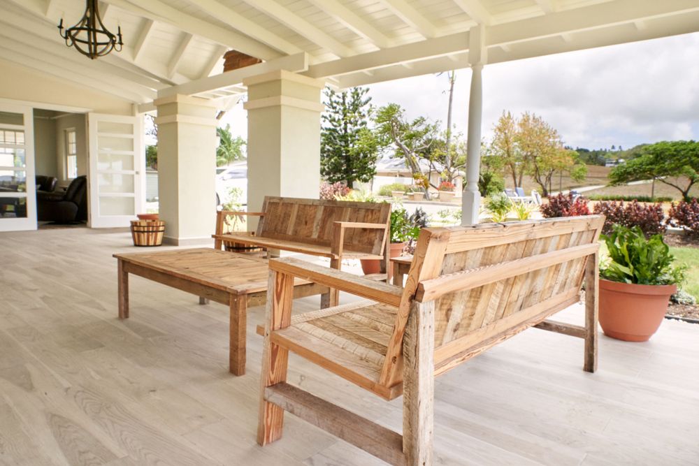 Covered patio area with wooden benches and white columns overlooking a tropical landscape.
