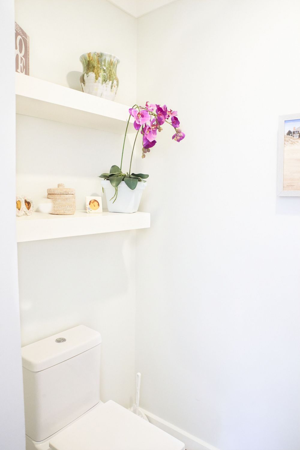 Minimalist white bathroom interior with built-in shelves displaying orchids and decor items.