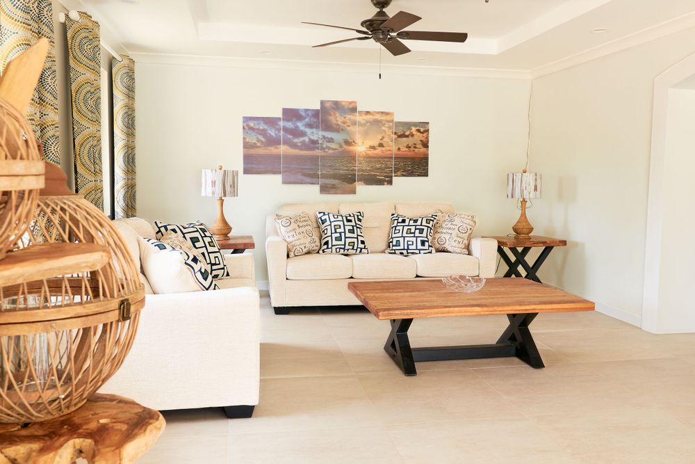 Spacious living room with white sofas, ceiling fan, and coastal artwork on walls.