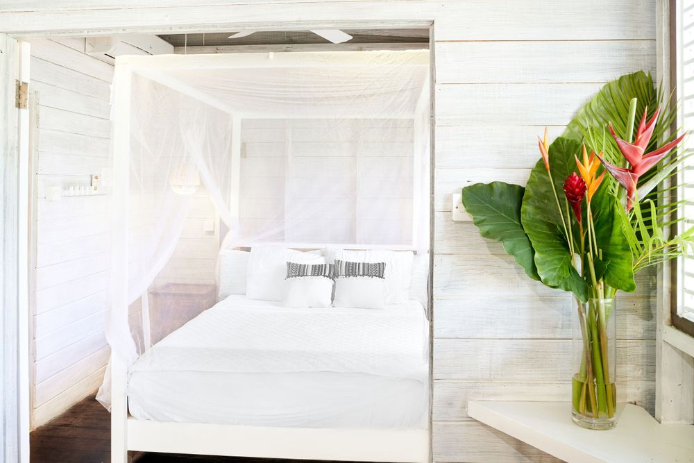 Bright white bedroom interior with tropical flower arrangements and flowing curtains.