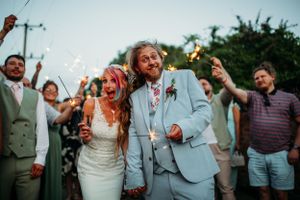 Evening wedding celebration with couple and guests holding sparklers on outdoor path.