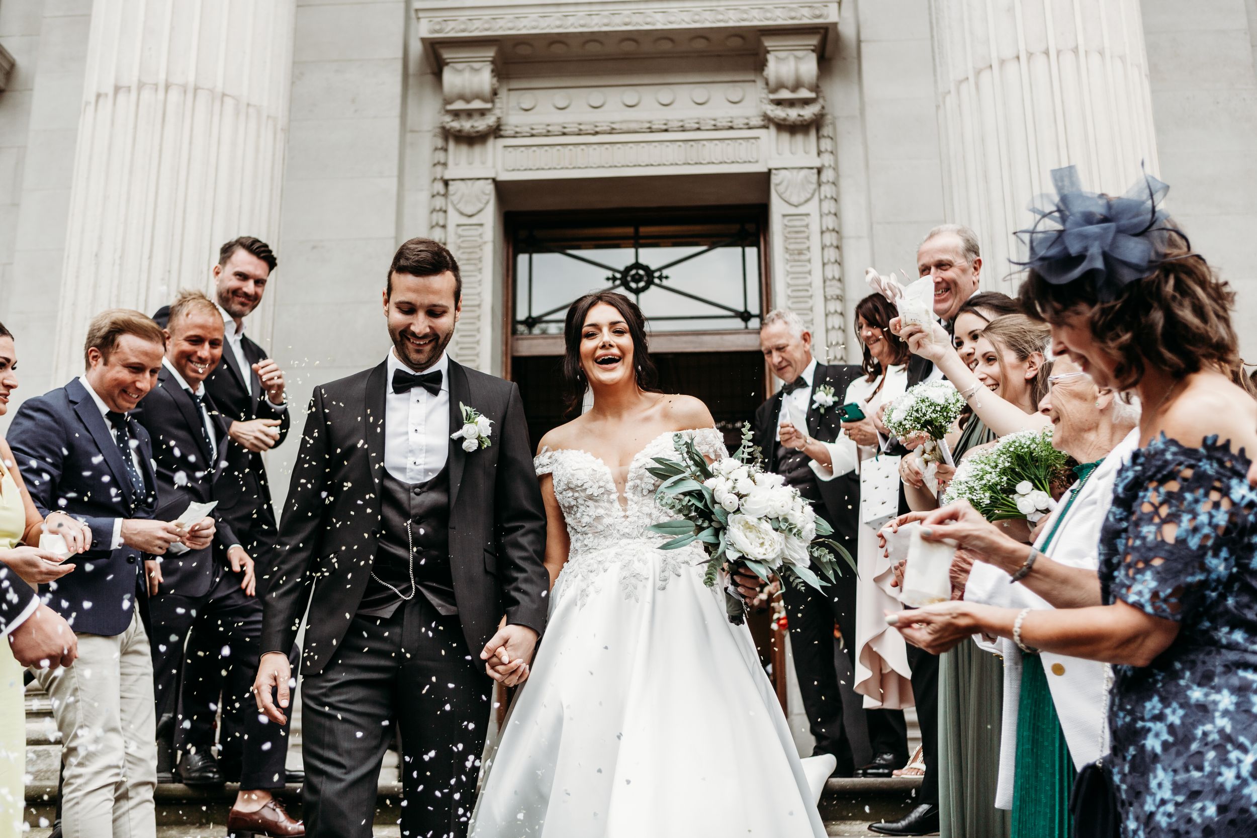 Wedding celebration with confetti shower on historic building steps.