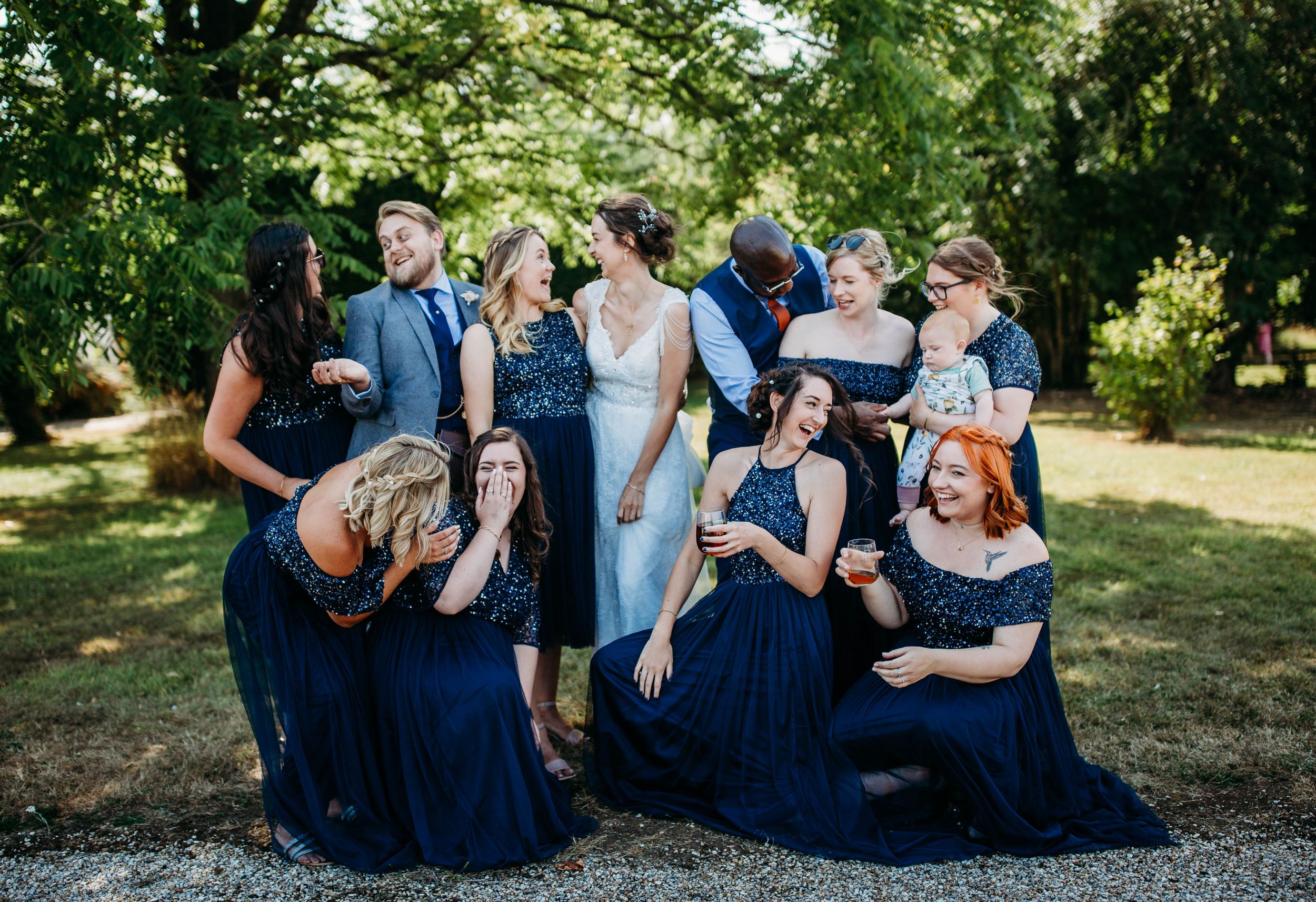 Bridesmaids in navy blue dresses sharing laughs during outdoor wedding photoshoot.