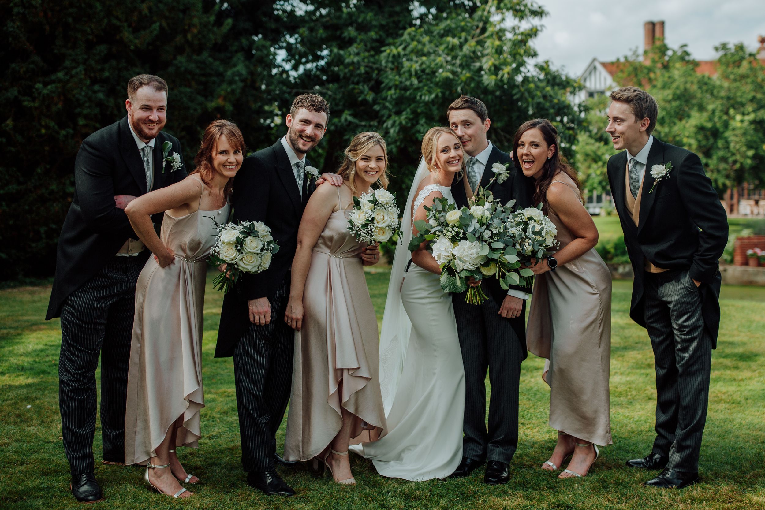 Wedding party posing outdoors with bouquets of white and green flowers.