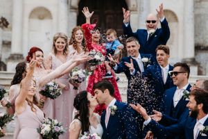 Wedding party celebrates with confetti toss on church steps.