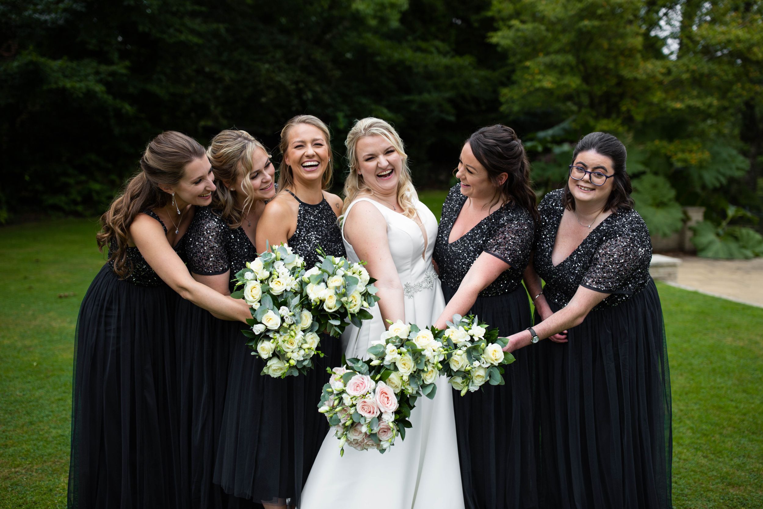 Wedding party in black dresses holding elegant white and green flower bouquets.