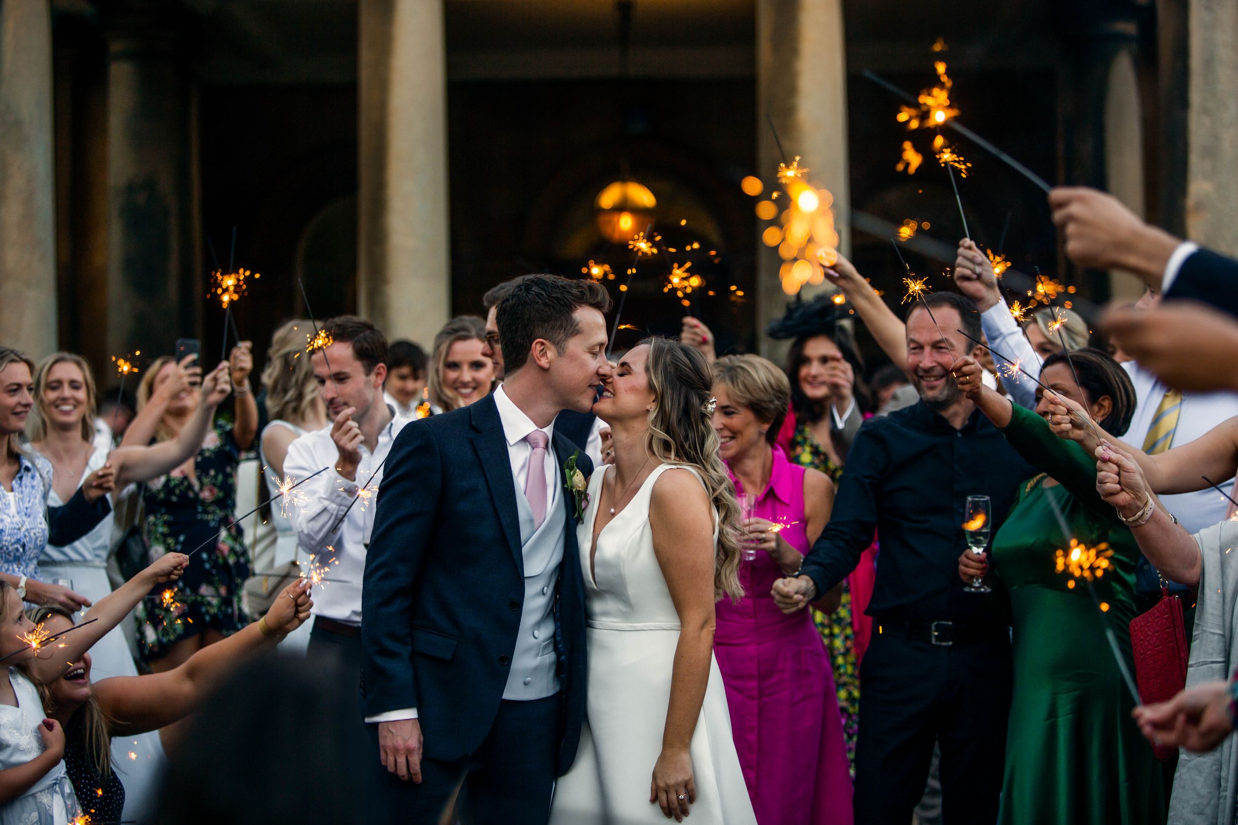 Wedding couple exits ceremony through sparkler tunnel lined with cheering guests.