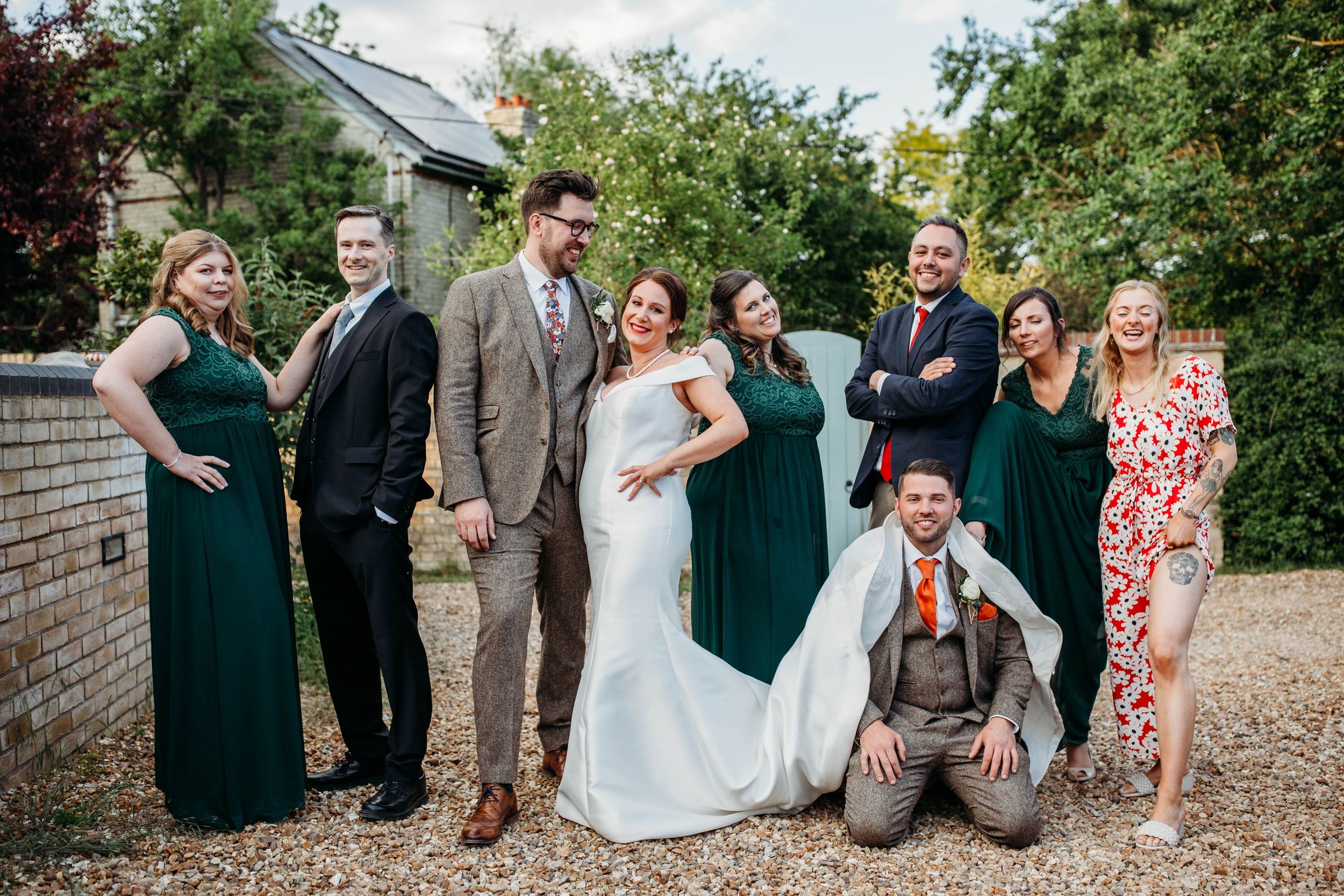 Wedding party poses outdoors in green and neutral attire on brick path.