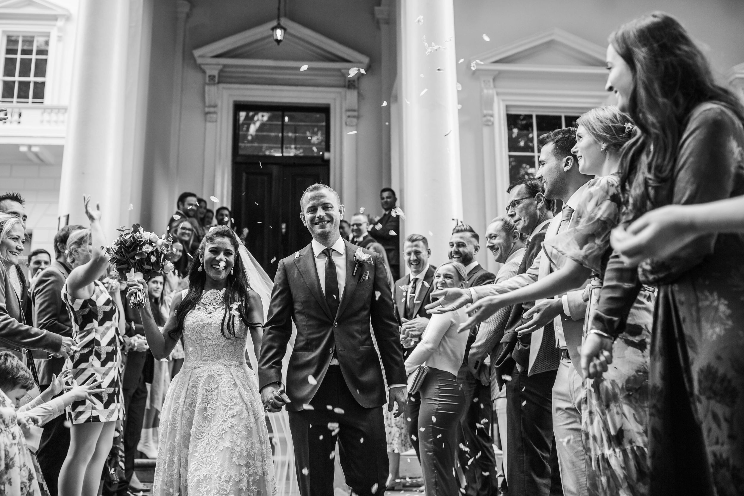 Wedding celebrants exit ceremony amid shower of confetti and cheering guests.