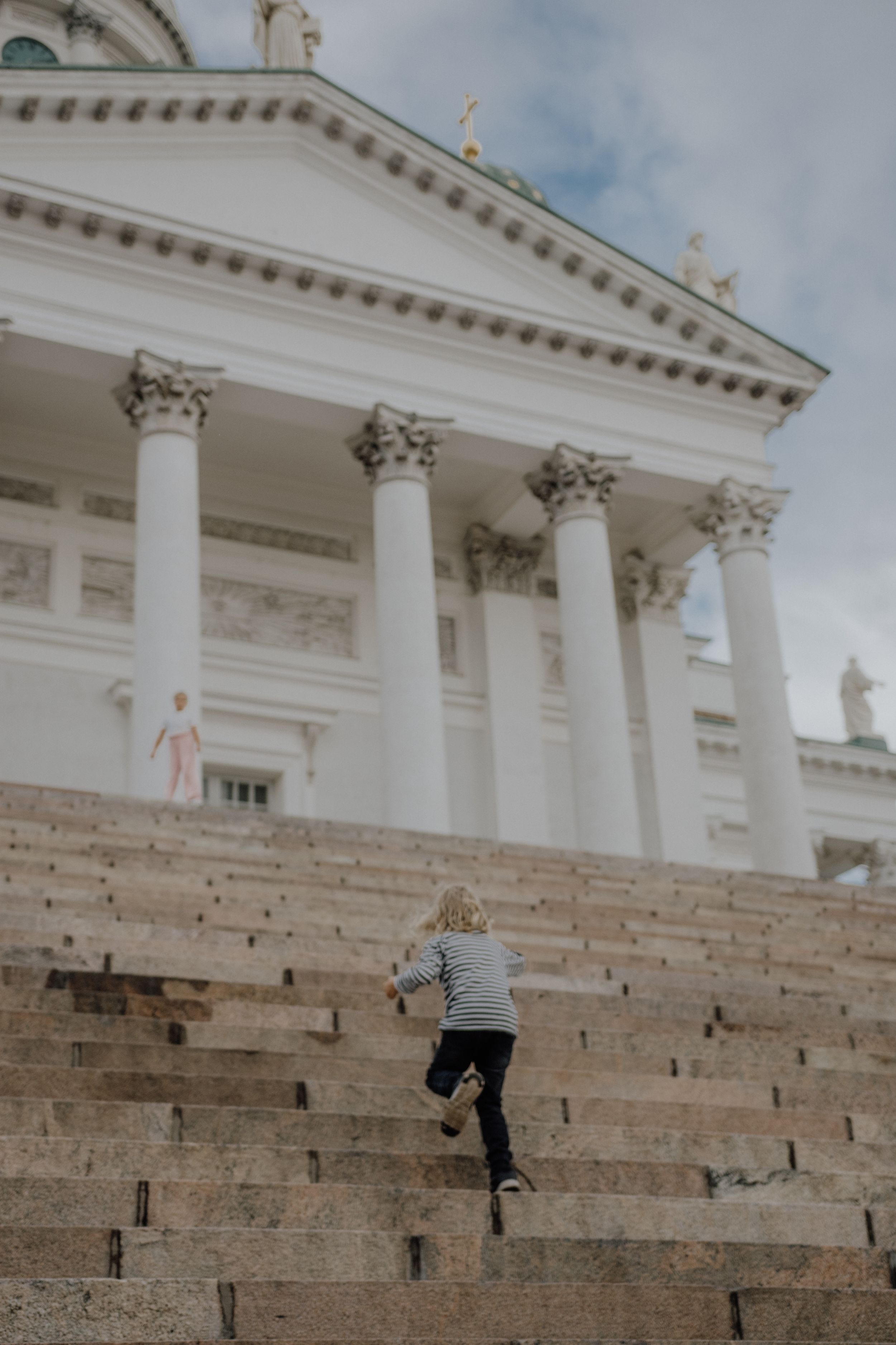 Person climbing steep stone steps of a grand neoclassical building with white columns.