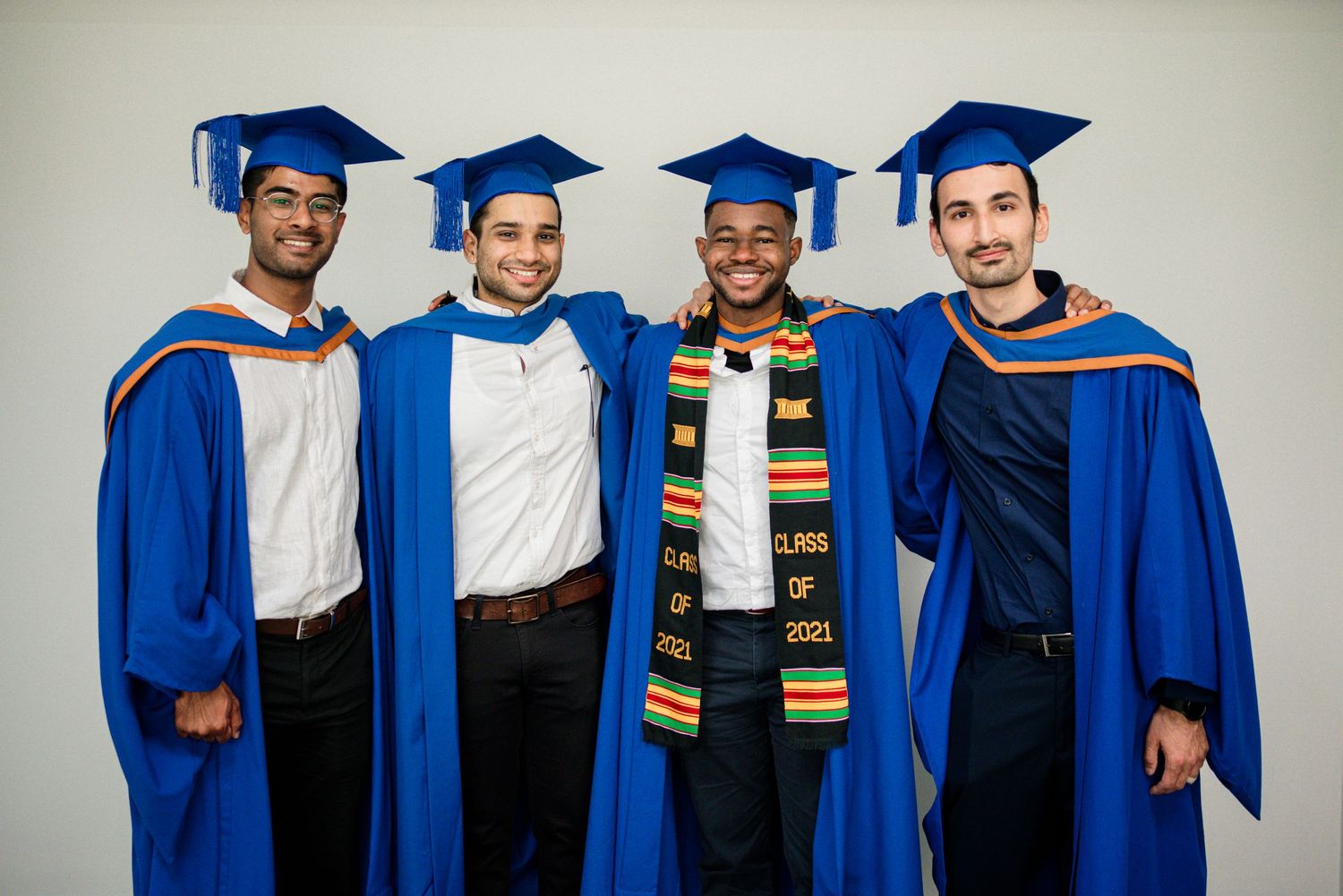 Graduates wearing bright blue gowns and caps line up wearing decorative stoles and medals.