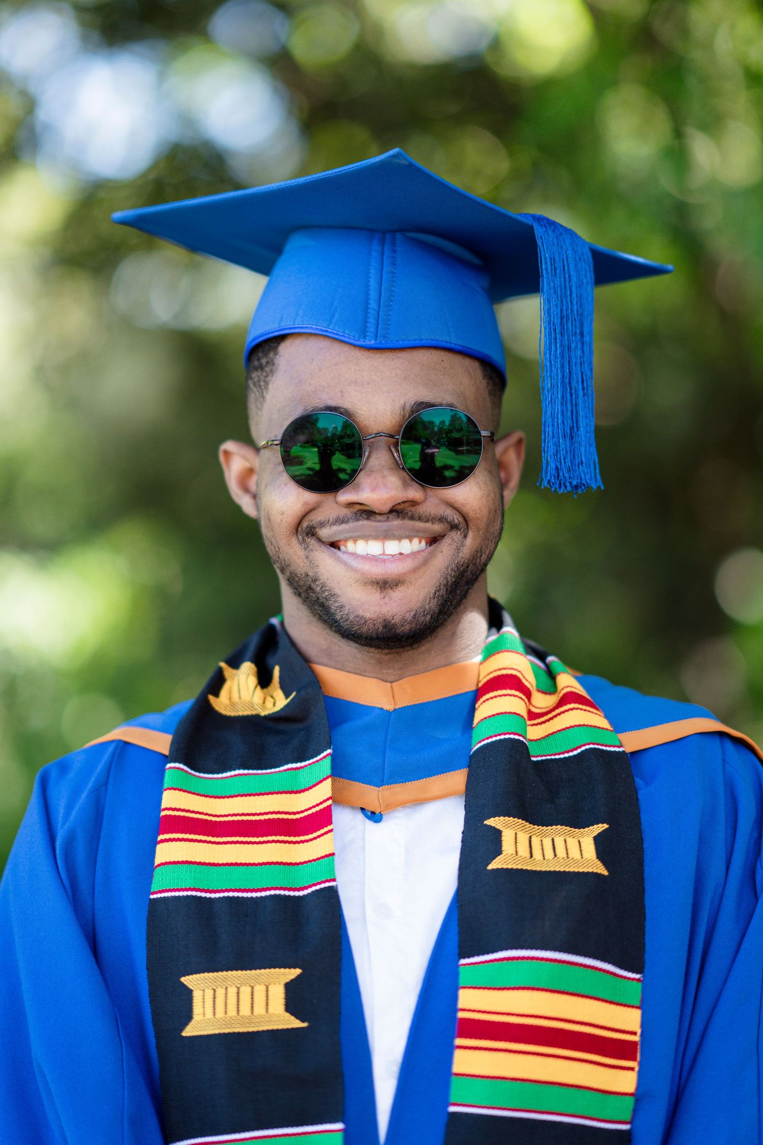 Graduate wearing traditional stole and blue graduation attire poses with joyful expression.