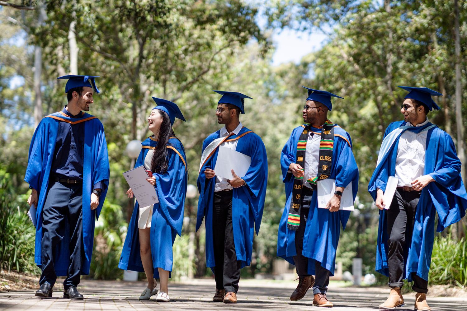 Graduates in blue robes celebrate together during outdoor commencement ceremony.