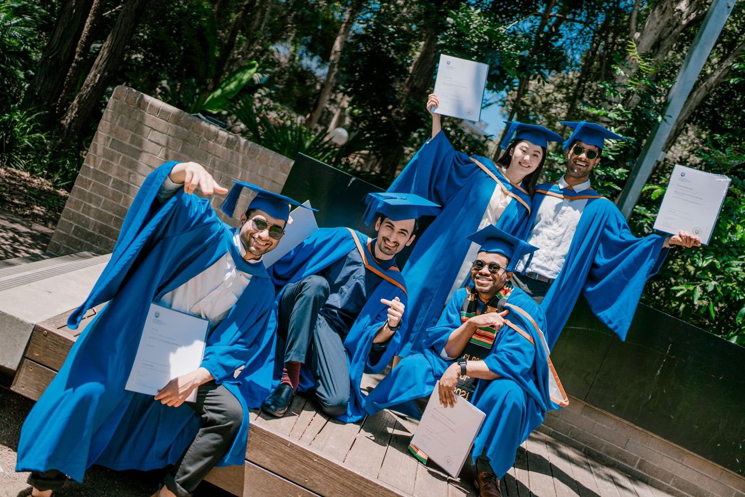 Graduates in bright blue robes share joyful moments during commencement photo session.