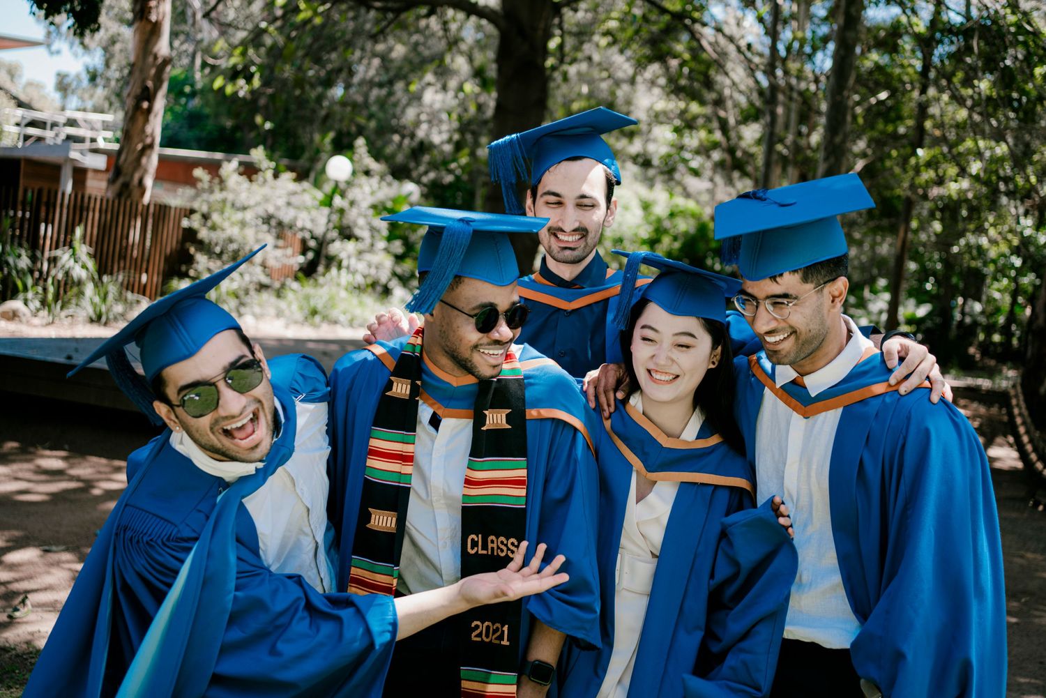 Students in blue graduation robes celebrate together during outdoor photo session.