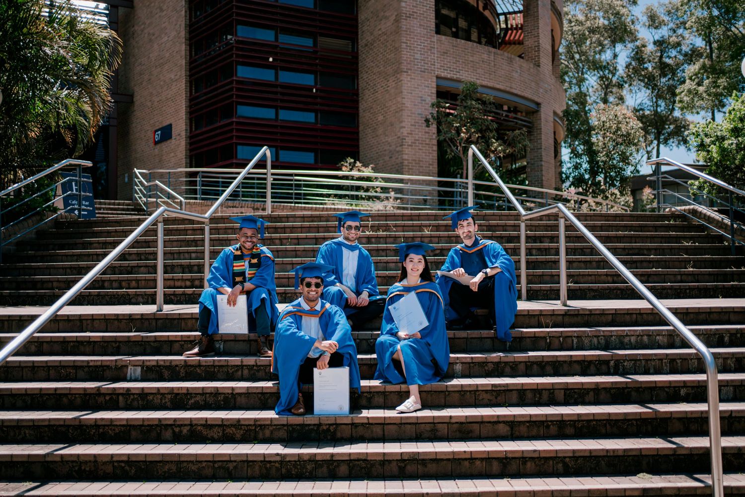 Graduates sitting and posing playfully on wide stone steps of a building.