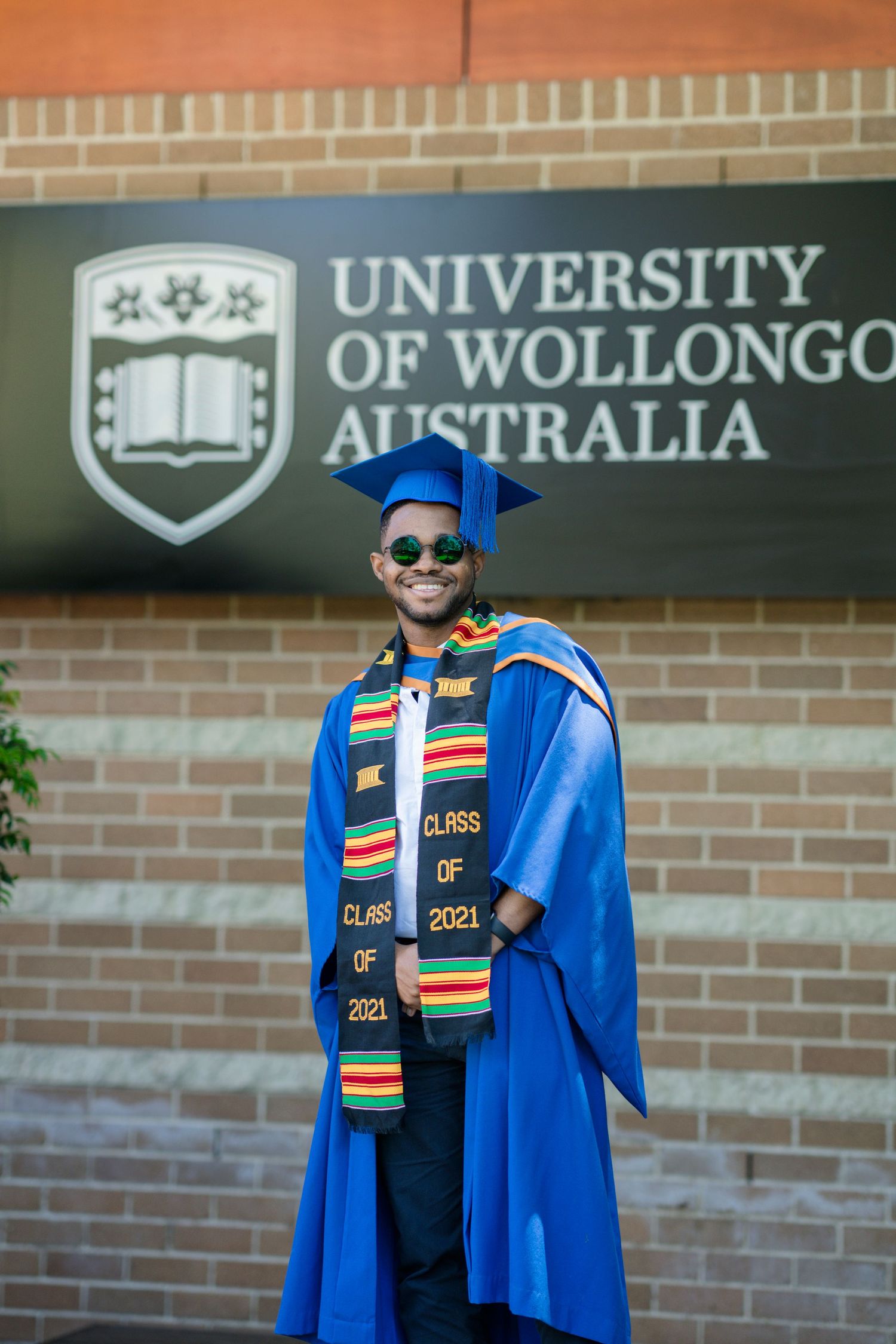Graduate in blue academic regalia and colorful stole posing at University of Wollongong.