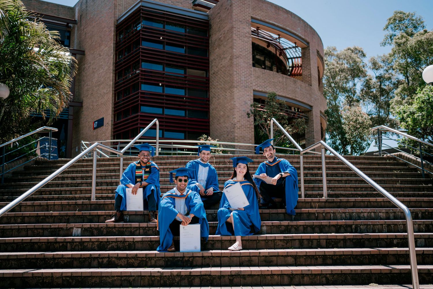 Graduates in bright blue gowns congregate on architectural steps for photos.