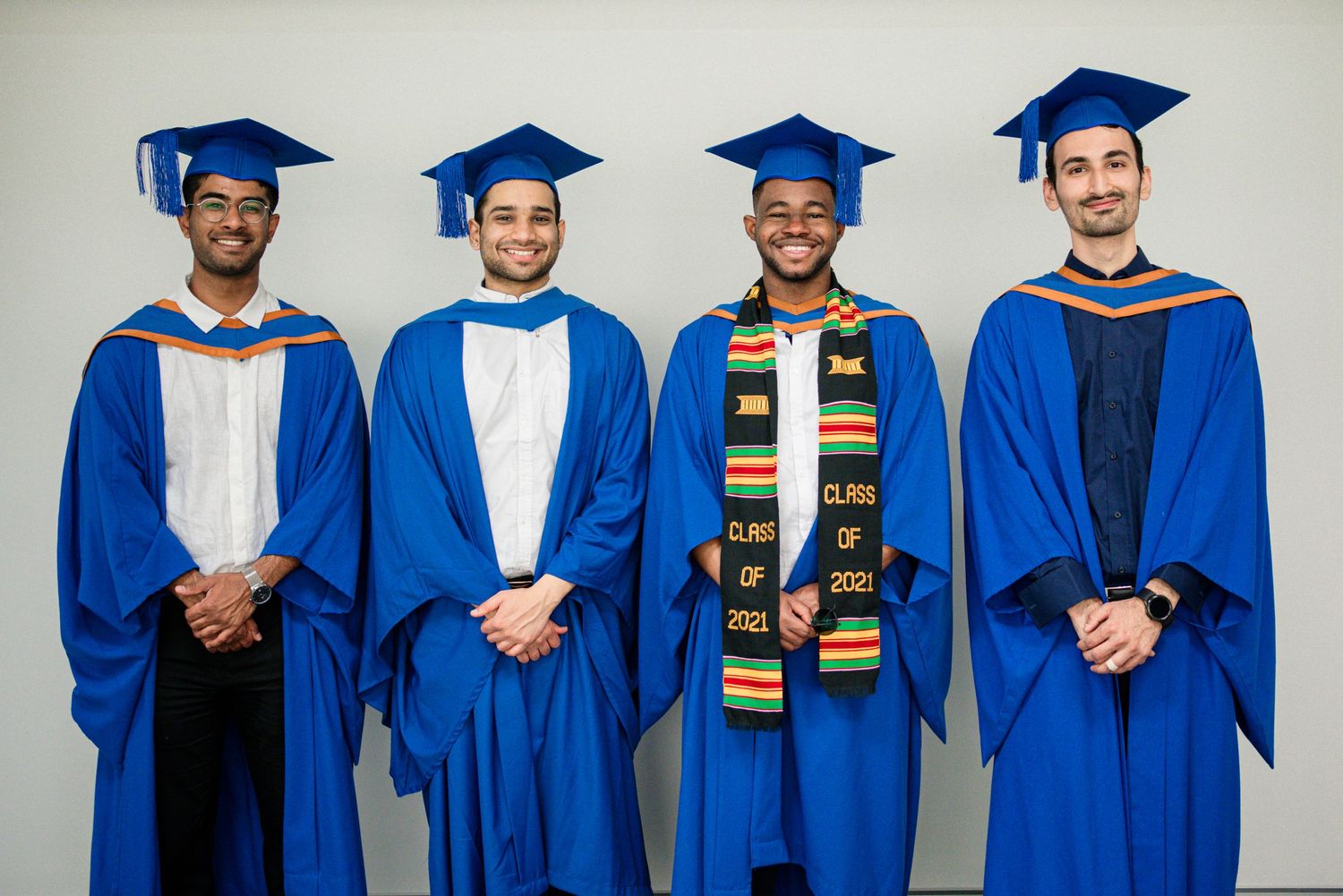 Graduates in blue academic regalia and colorful stoles pose together for a formal group photo.