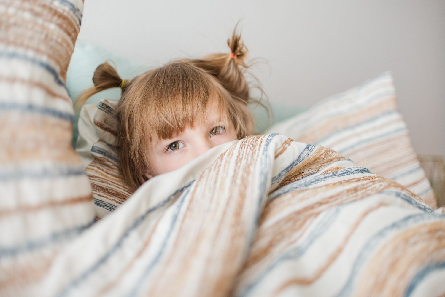 Child peeking over striped bedding with playful expression.