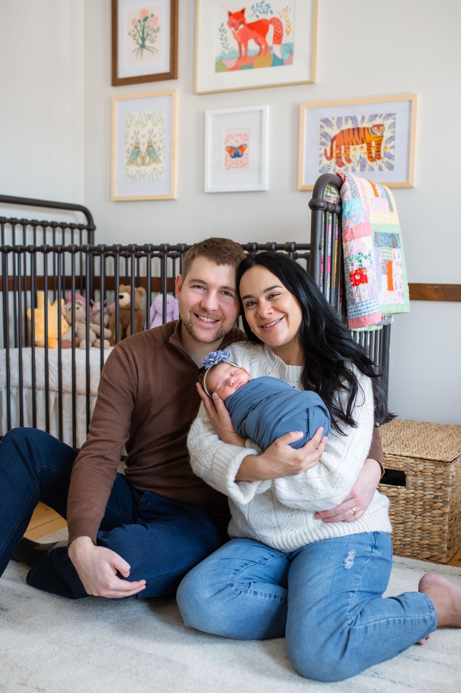 Family cuddles with newborn in nursery decorated with whimsical animal artwork.