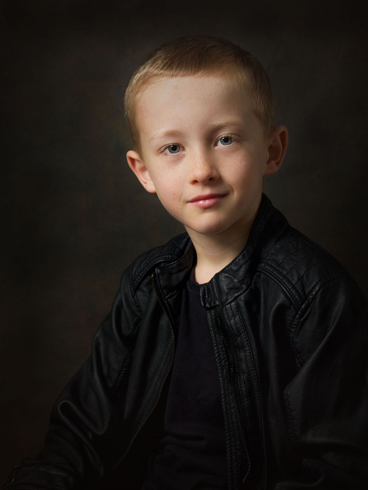 portrait of fair haired young boy wear black leather jacket with smile