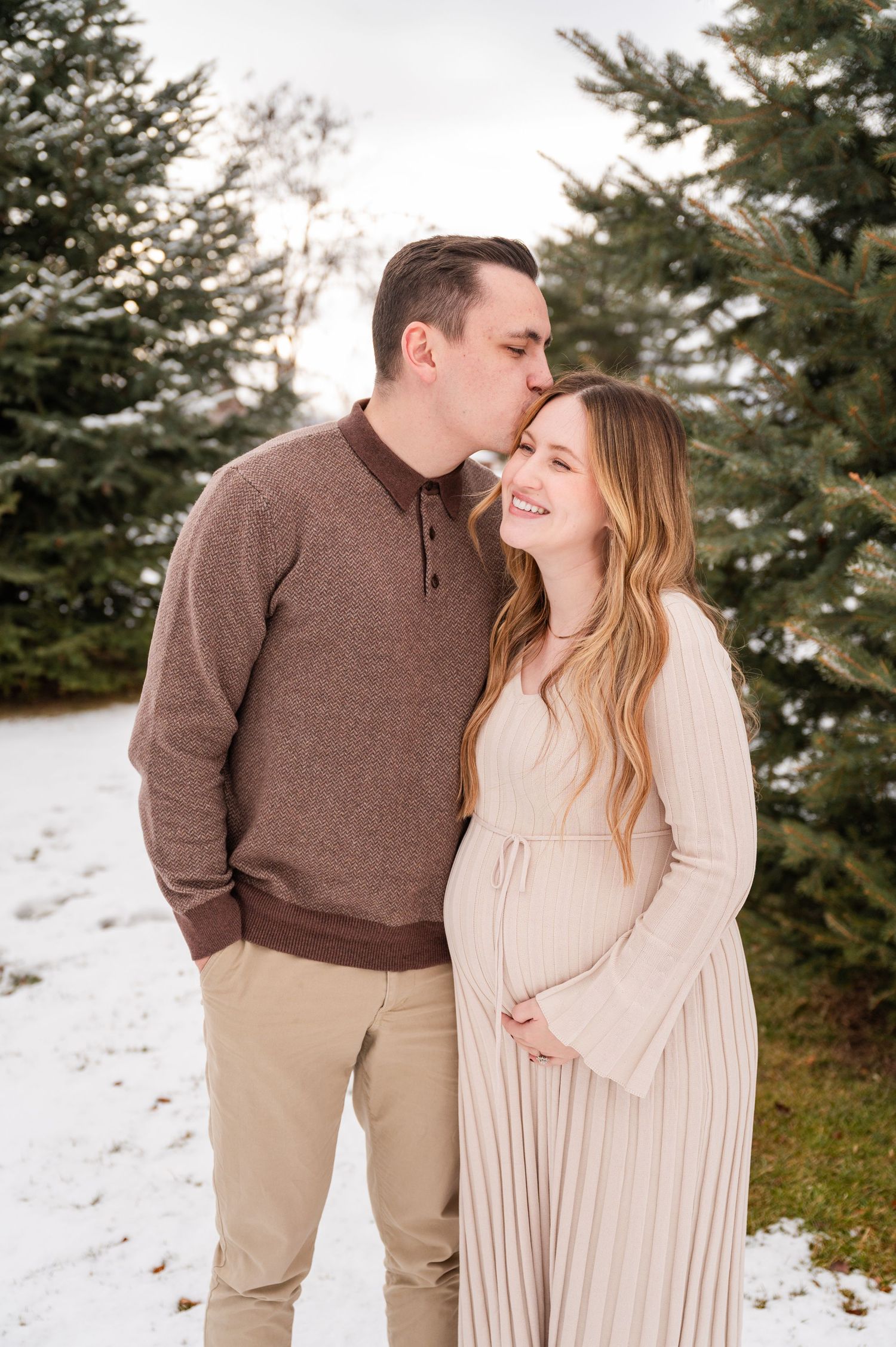 Couple shares tender moment in snowy winter scene with evergreen trees in background.
