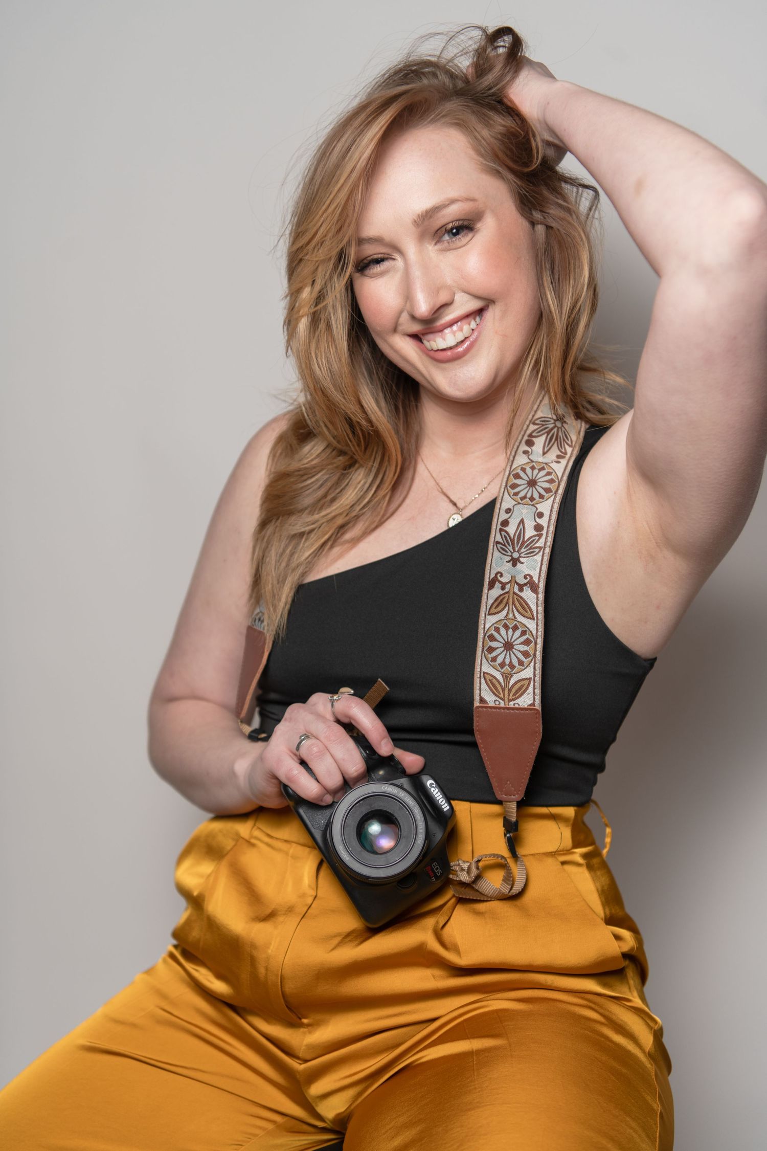 Portrait of photographer with camera wearing black top and yellow pants.