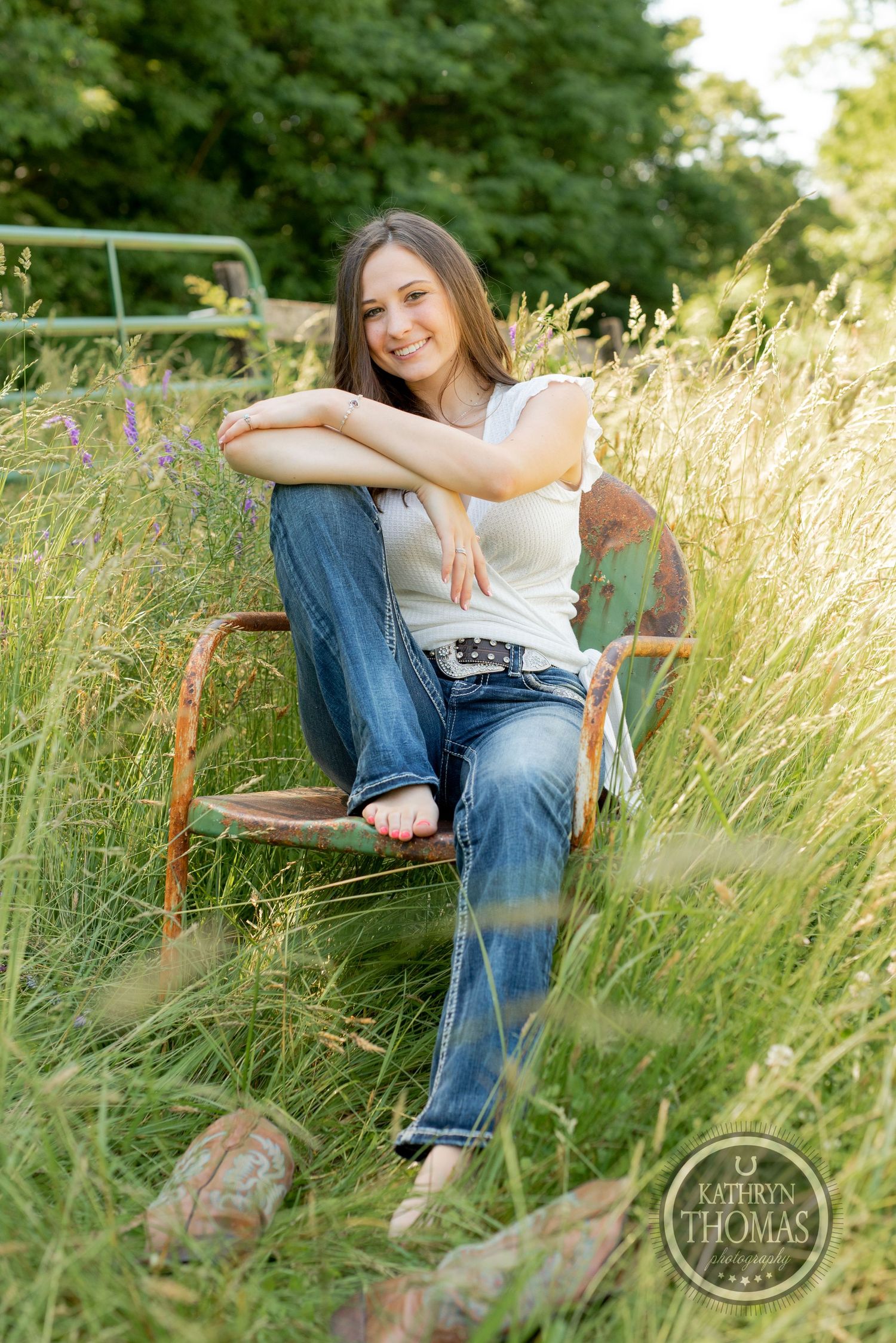 Relaxed outdoor portrait in tall grass with vintage metal chair and casual summer outfit.