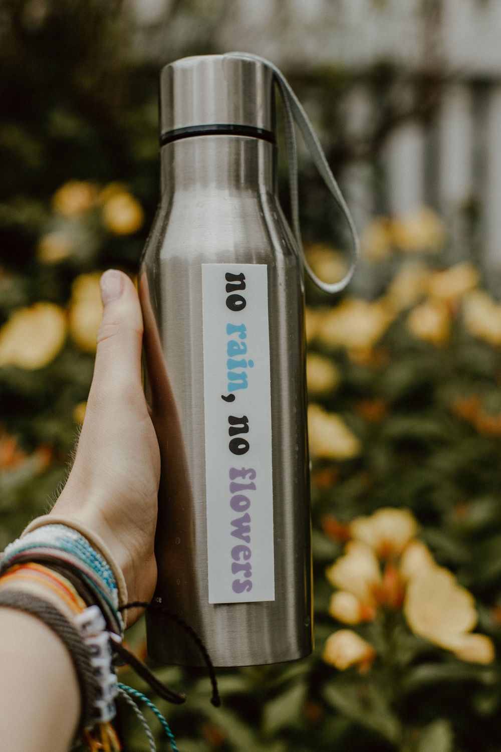Hand holding stainless steel water bottle with text label against autumn leaves background.